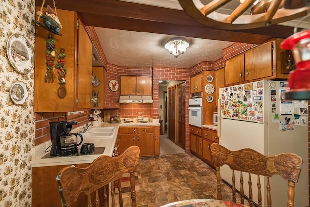 kitchen featuring white appliances, sink, and brick wall