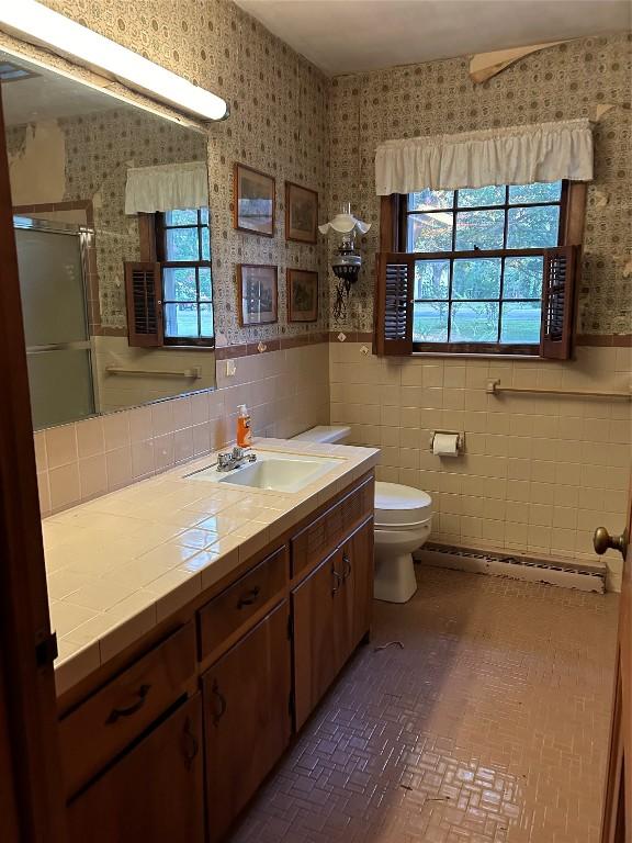 bathroom featuring vanity, a baseboard radiator, tile walls, toilet, and a shower with shower door