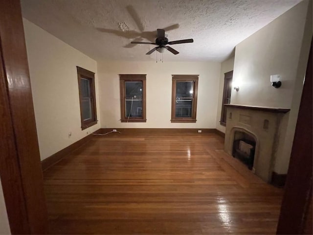 unfurnished living room with a fireplace, ceiling fan, dark hardwood / wood-style flooring, and a textured ceiling