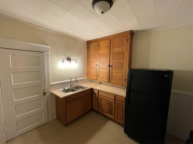 kitchen featuring black refrigerator, crown molding, light tile patterned floors, and sink