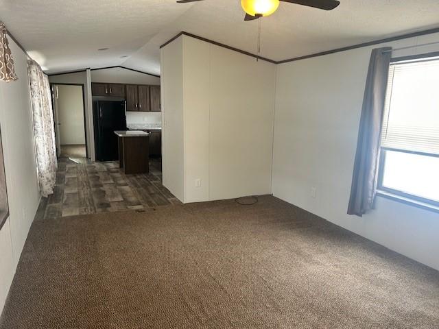 unfurnished living room featuring ceiling fan, lofted ceiling, and dark colored carpet