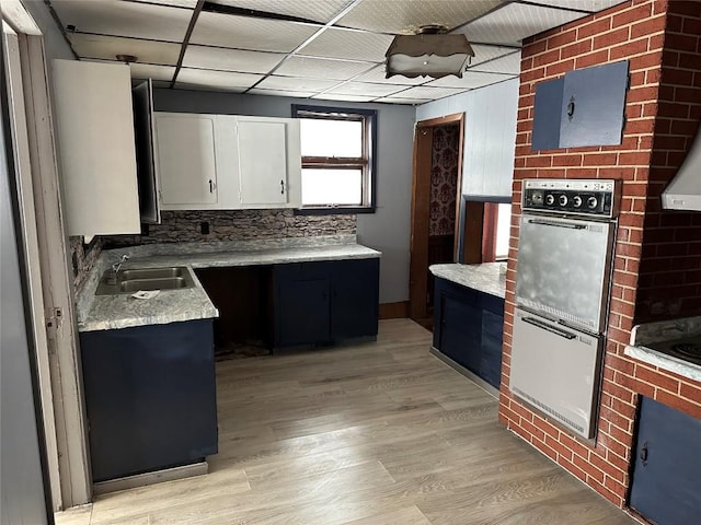 kitchen with white cabinetry, a drop ceiling, sink, tasteful backsplash, and light wood-type flooring