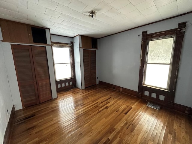 unfurnished bedroom featuring multiple windows, multiple closets, ornamental molding, and hardwood / wood-style flooring