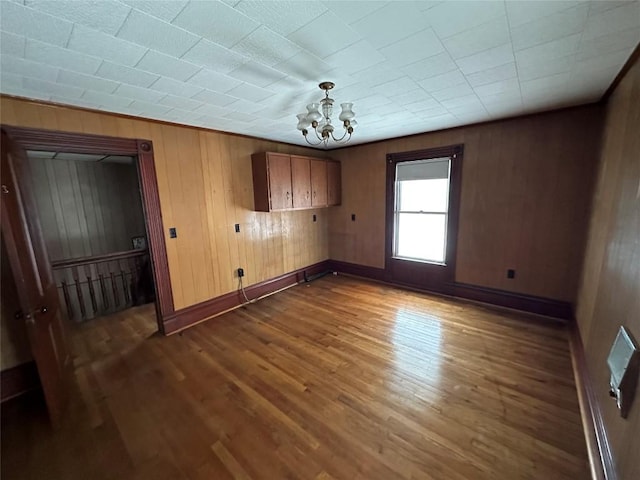 unfurnished room featuring dark wood-type flooring, wooden walls, and a chandelier