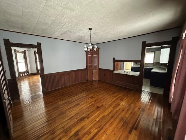 unfurnished dining area featuring dark hardwood / wood-style flooring, ornamental molding, and an inviting chandelier