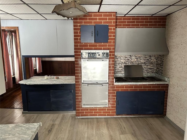 kitchen featuring hardwood / wood-style floors, a paneled ceiling, light stone countertops, and multiple ovens