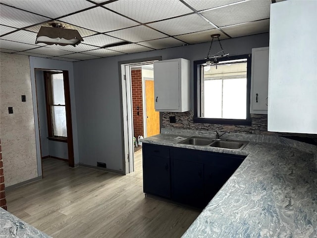 kitchen featuring white cabinetry, sink, hanging light fixtures, tasteful backsplash, and light hardwood / wood-style floors