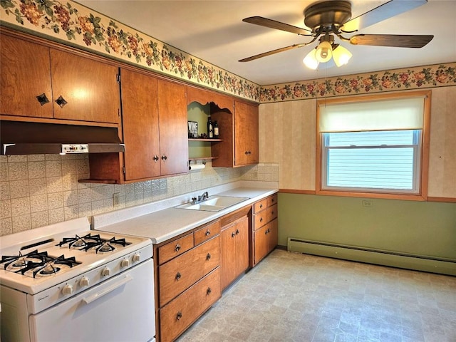 kitchen featuring baseboard heating, brown cabinets, a sink, under cabinet range hood, and white range with gas stovetop