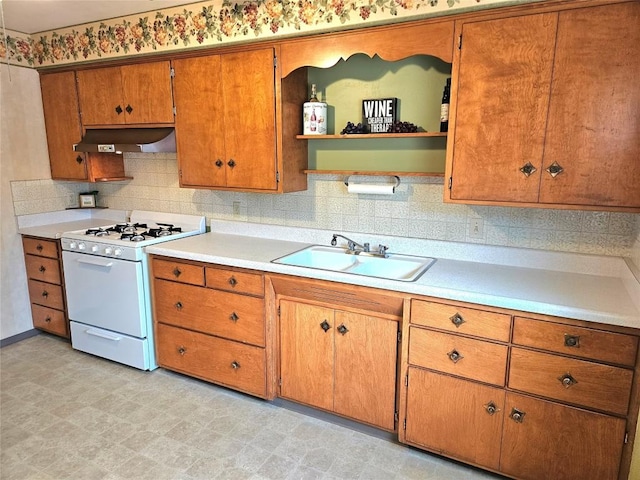 kitchen with white gas range, open shelves, brown cabinets, a sink, and under cabinet range hood