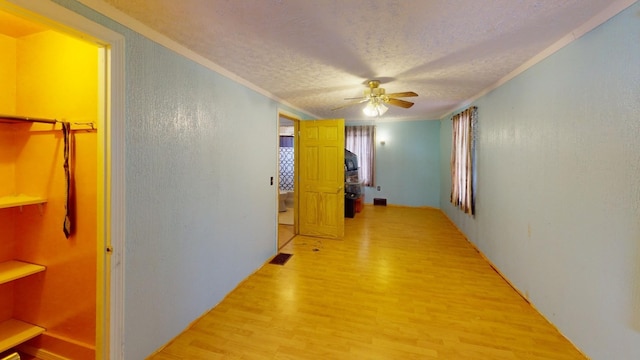 corridor with light hardwood / wood-style floors, a textured ceiling, and ornamental molding