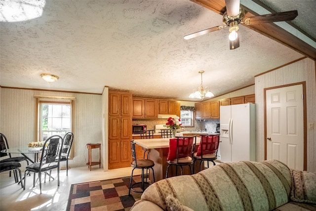 kitchen featuring white fridge with ice dispenser, pendant lighting, a breakfast bar, a kitchen island, and ceiling fan with notable chandelier