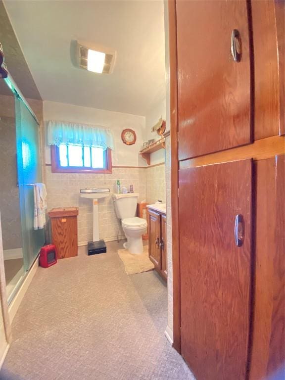 bathroom featuring toilet, a shower with door, and tile walls