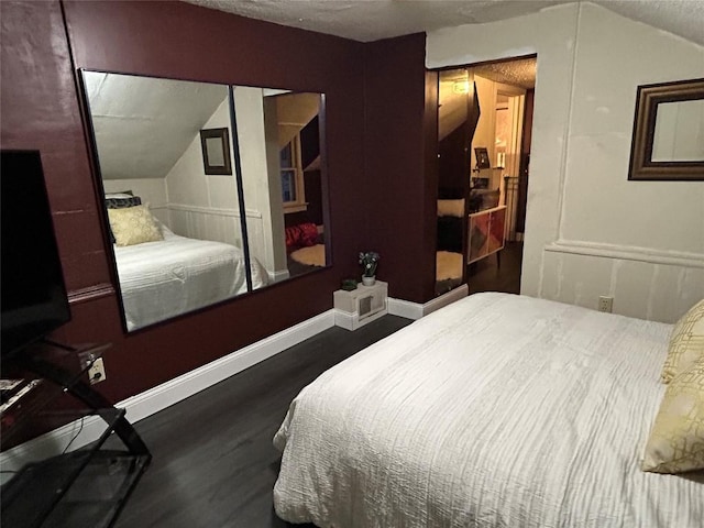 bedroom with a textured ceiling, vaulted ceiling, and dark wood-type flooring