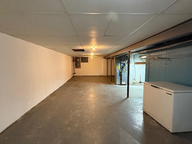 basement with a paneled ceiling, electric panel, refrigerator, and heating unit