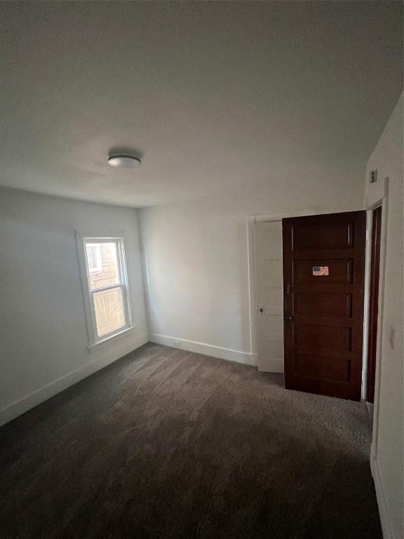 spare room featuring dark colored carpet and baseboards