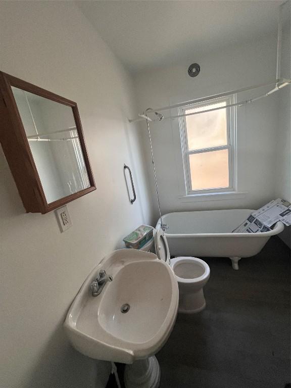 full bath with a soaking tub, toilet, and a sink