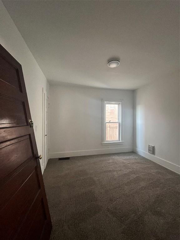 empty room featuring dark colored carpet, visible vents, and baseboards