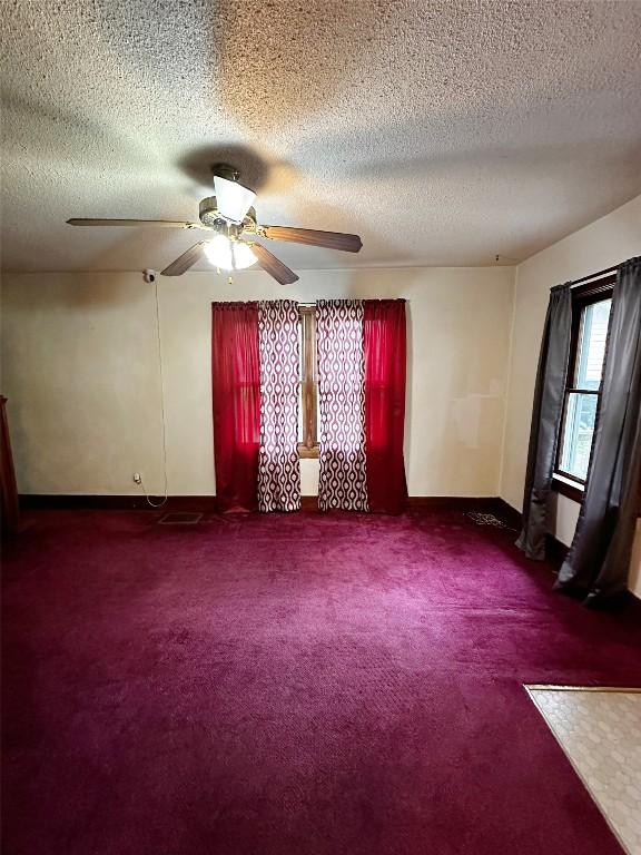 spare room featuring a ceiling fan, baseboards, dark carpet, and a textured ceiling