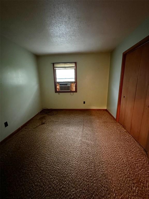 unfurnished bedroom with baseboards, a textured ceiling, carpet, and cooling unit