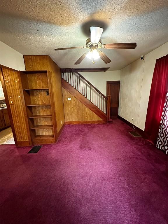 interior space featuring a textured ceiling, ceiling fan, and dark carpet