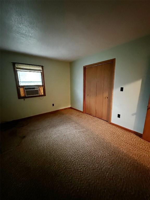 unfurnished bedroom with carpet flooring, a closet, baseboards, and cooling unit