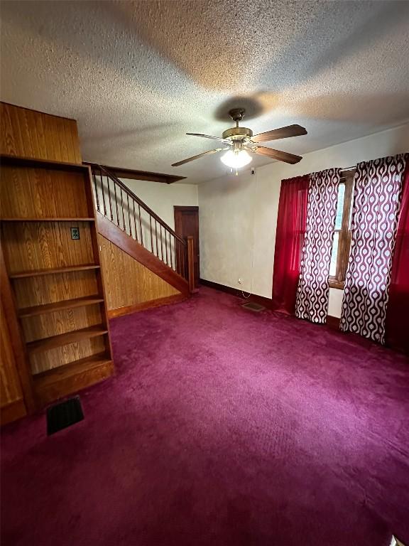 unfurnished living room with carpet flooring, a textured ceiling, a ceiling fan, and stairway
