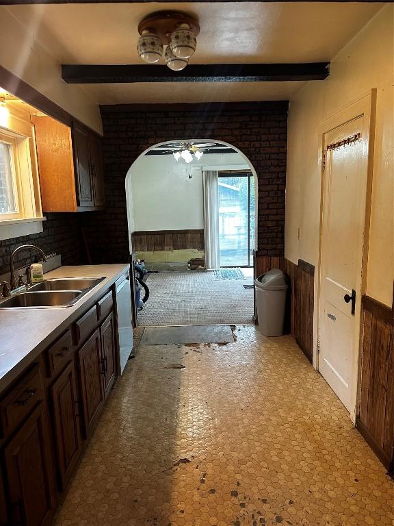 kitchen featuring a ceiling fan, beam ceiling, a wainscoted wall, a sink, and dishwasher