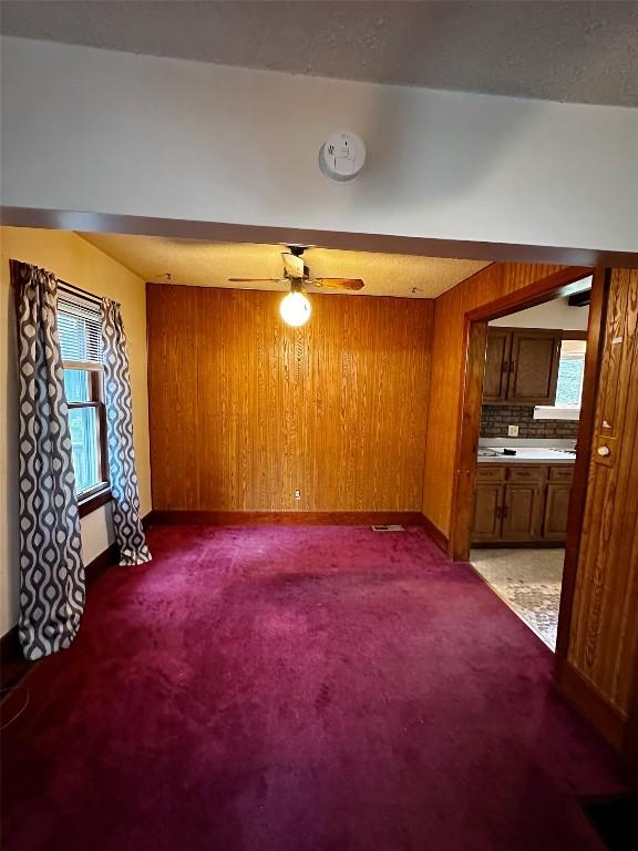 unfurnished living room featuring baseboards, wood walls, ceiling fan, and a wealth of natural light