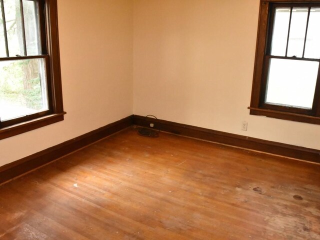 unfurnished room featuring baseboards, wood finished floors, and a healthy amount of sunlight