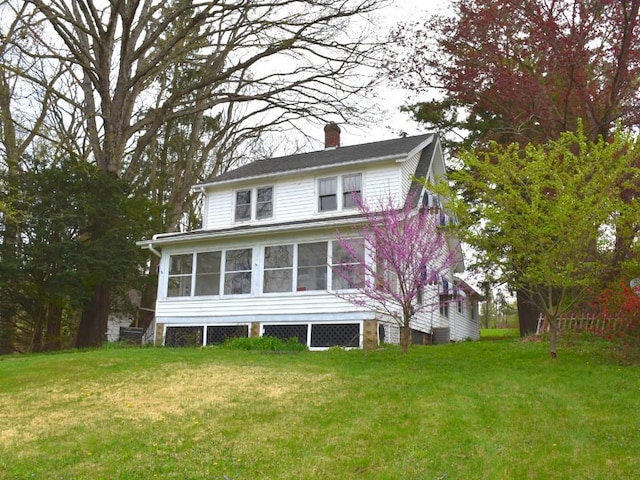 rear view of house featuring a lawn, a chimney, and a sunroom