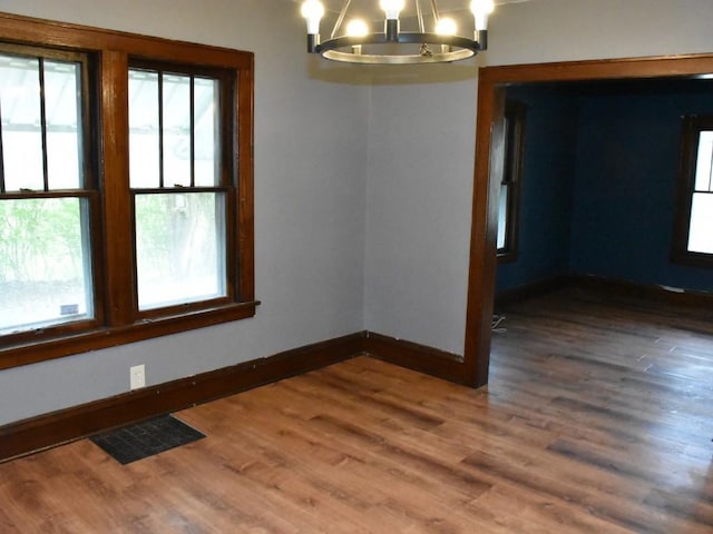 spare room featuring baseboards, wood finished floors, a notable chandelier, and visible vents