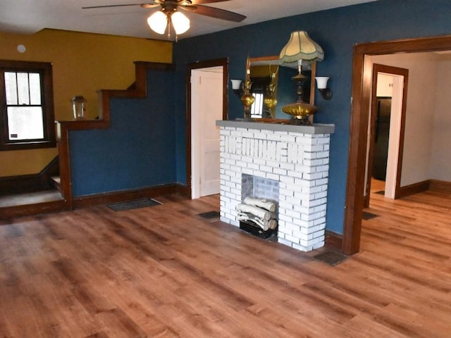 unfurnished living room featuring ceiling fan, a fireplace, baseboards, wood finished floors, and visible vents