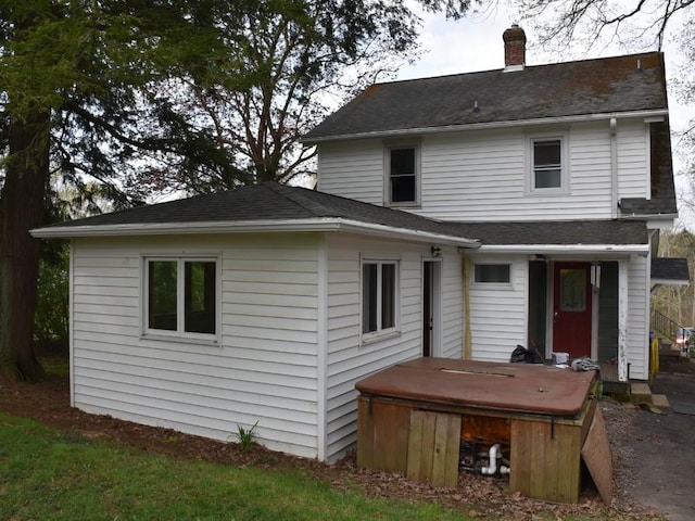 rear view of house with a shingled roof, a covered hot tub, and a chimney