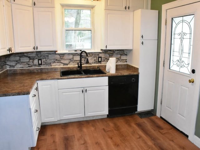 kitchen with dark countertops, a sink, dishwasher, white cabinetry, and decorative backsplash
