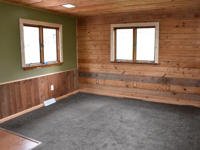 empty room with wood walls, wooden ceiling, and dark colored carpet