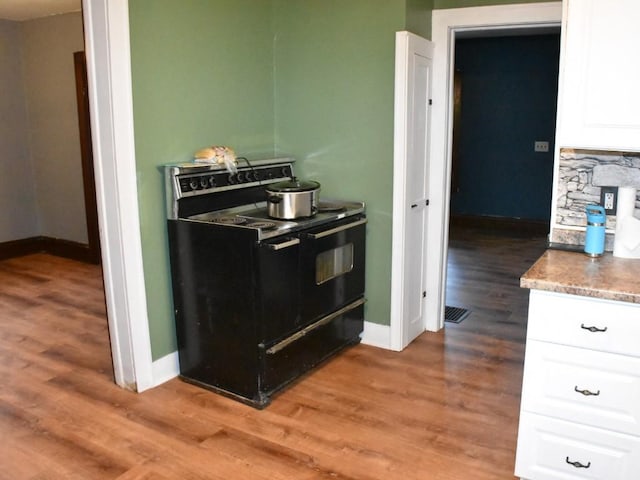 kitchen with white cabinetry, light wood-style floors, baseboards, and black range with electric stovetop