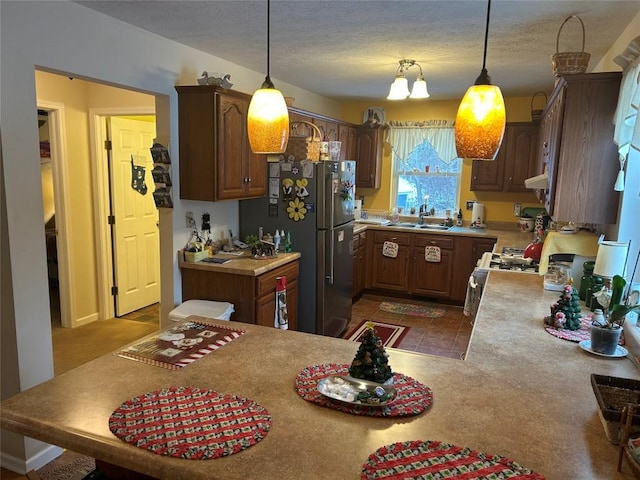 kitchen featuring kitchen peninsula, stainless steel fridge, hanging light fixtures, and sink