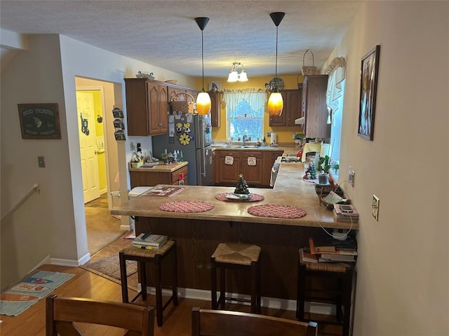 kitchen with a breakfast bar, light hardwood / wood-style flooring, stainless steel fridge, decorative light fixtures, and kitchen peninsula