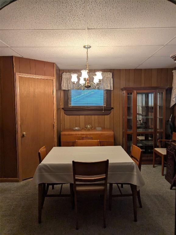 dining room featuring an inviting chandelier, wooden walls, and carpet flooring