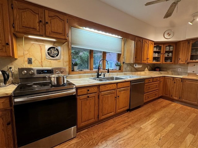 kitchen featuring appliances with stainless steel finishes, sink, backsplash, ceiling fan, and light hardwood / wood-style flooring