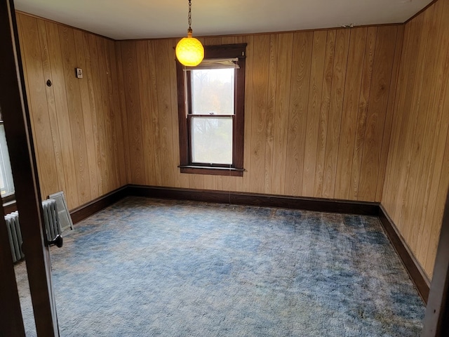 spare room with wood walls, dark carpet, and radiator