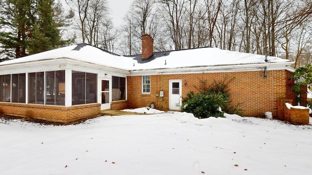 snow covered back of property featuring a sunroom