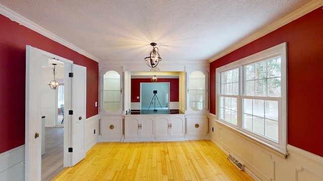 interior space featuring a textured ceiling, light wood-type flooring, and ornamental molding