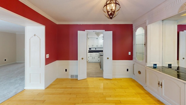 corridor with crown molding, light wood-type flooring, and a notable chandelier