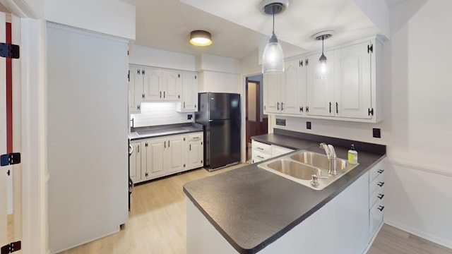 kitchen with kitchen peninsula, white cabinetry, black refrigerator, and sink