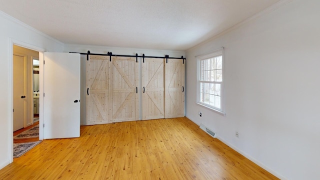 unfurnished bedroom featuring hardwood / wood-style floors, a barn door, ornamental molding, and a closet