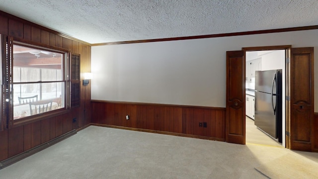 carpeted spare room featuring crown molding, a textured ceiling, and wooden walls