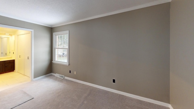 unfurnished bedroom with connected bathroom, light carpet, a textured ceiling, and ornamental molding