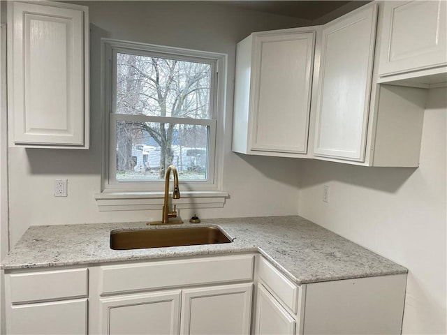 kitchen featuring light stone countertops, sink, and white cabinets