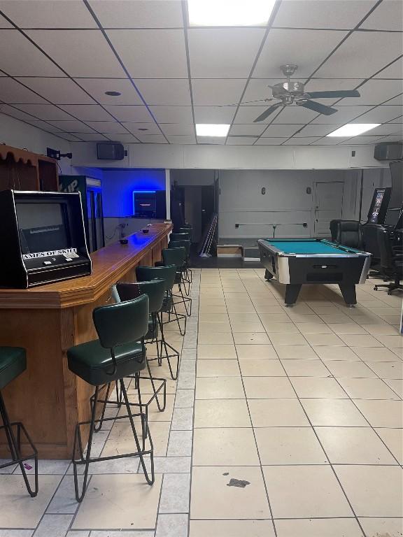 rec room with a paneled ceiling, billiards, indoor bar, light tile patterned floors, and ceiling fan